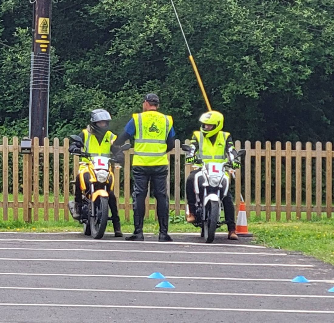 An instructor in hi-vis with two learner riders on L-plated training bikes on the manoeuvring pad at North Tawton
